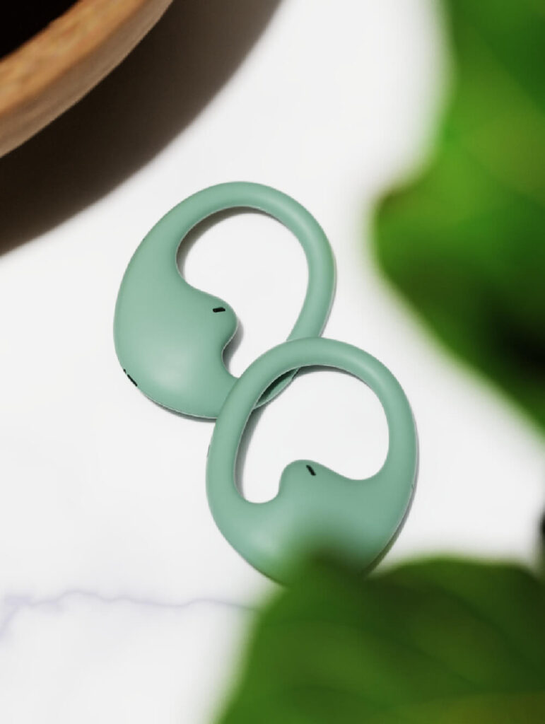 Two green ring like objects with a sleek design, amidst soft green leaves. Earbugs Headphones by All Design Lab